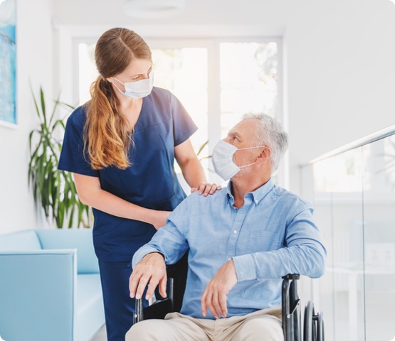 nurse and patient in wheelchair in medical face mask look at each other. There are in a Long-term care facility.