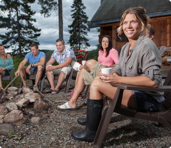 4 people sit outside beside a cottage with trees in the background